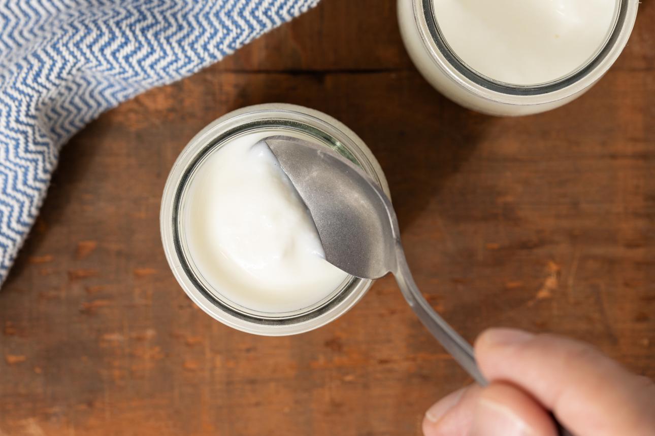 Creamy yogurt being scooped from a glass jar with a spoon on a rustic wooden table