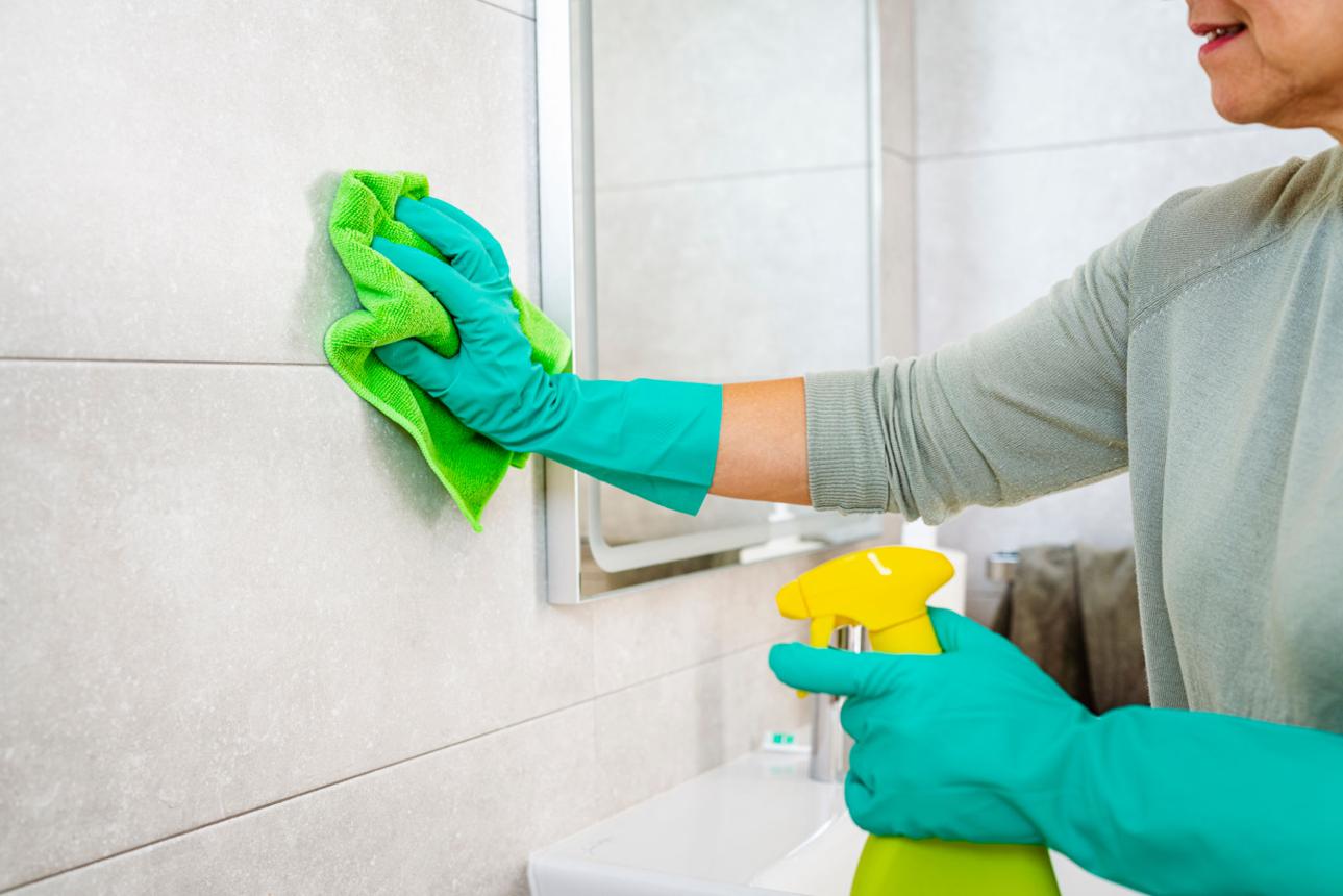Close up of woman's hands cleaning bathroom tiles with a microfiber cloth and spray cleaner