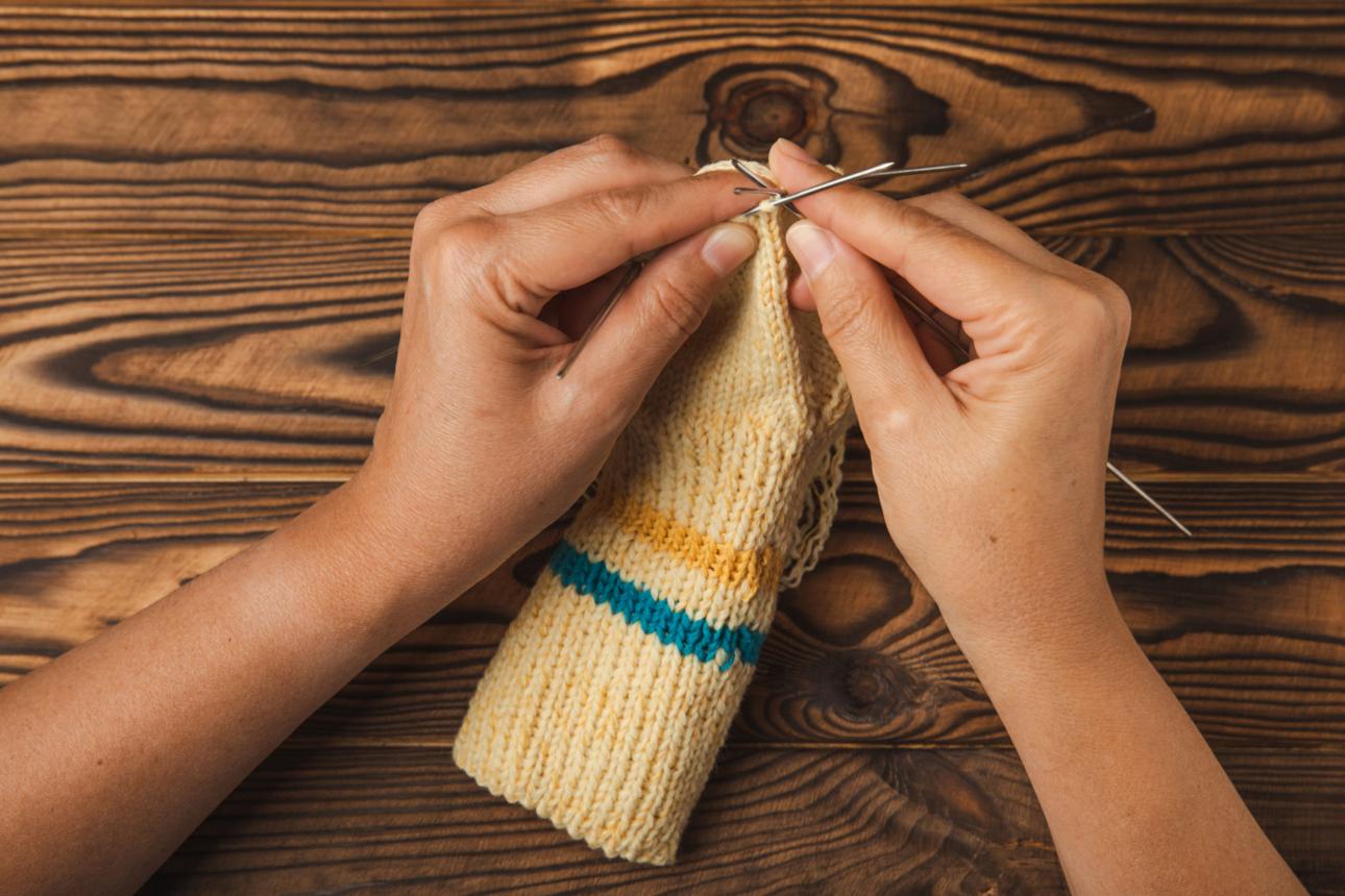 Knitting socks. work in progress. Woolen yarn in the hands of a woman on a brown texture wood. winter hobbies.Hobby.Place for text, space for copy.