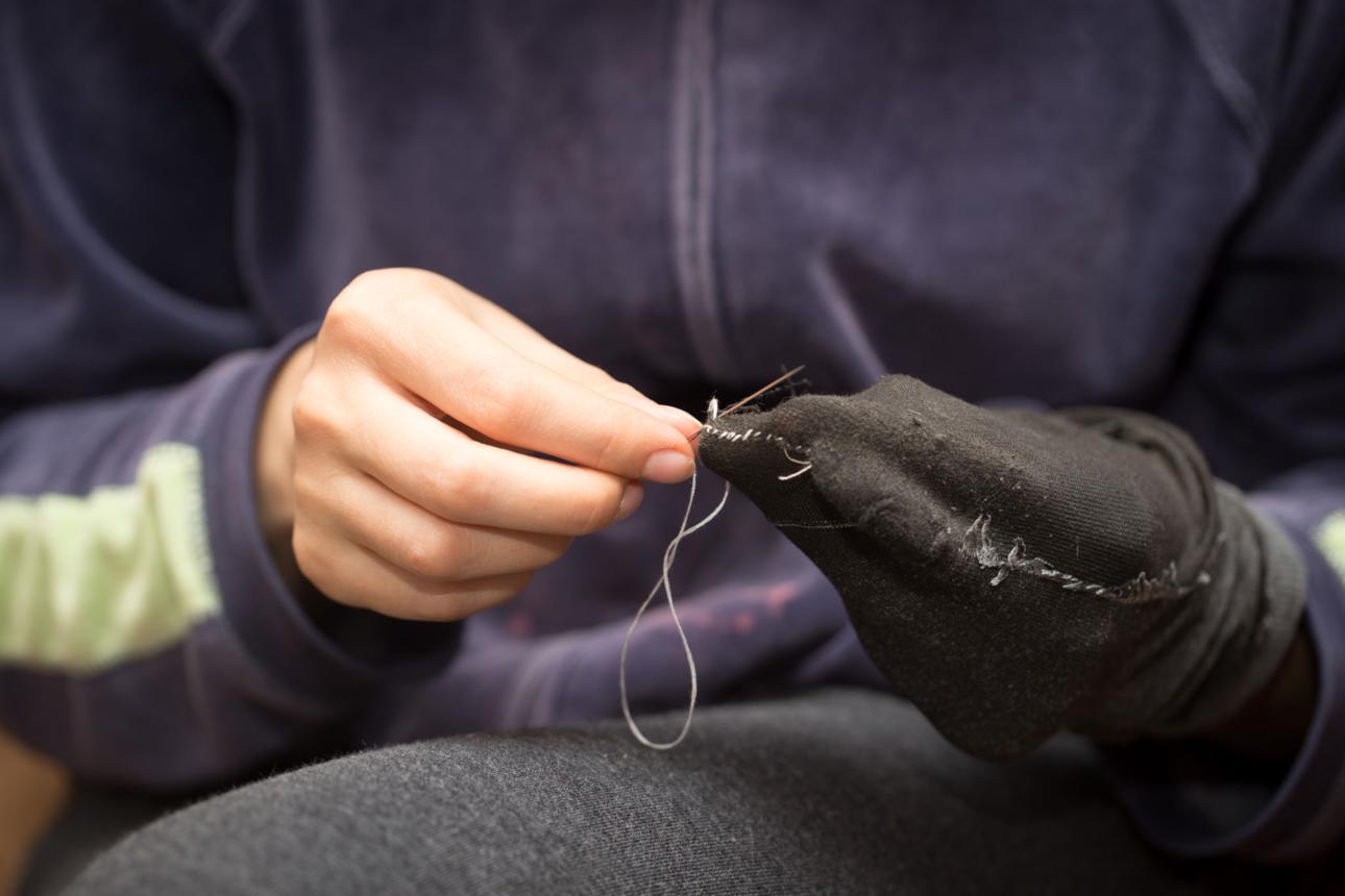 A girl sews a sock with a needle