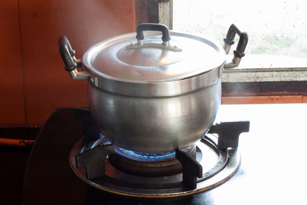 Cooking with aluminum pot on the gas stove in the kitchen with flame and smoke.