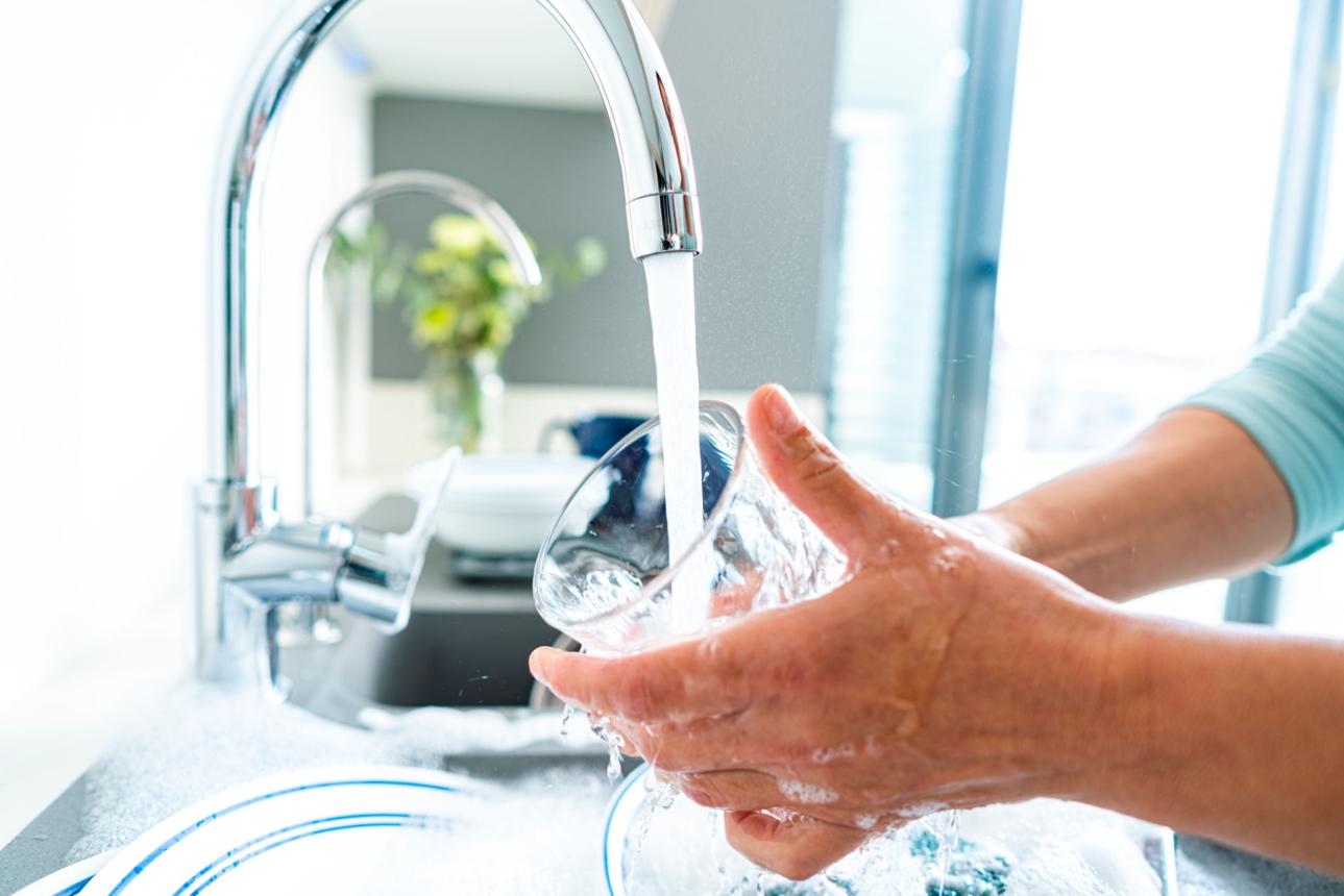 Woman washing a drinking glass under running water