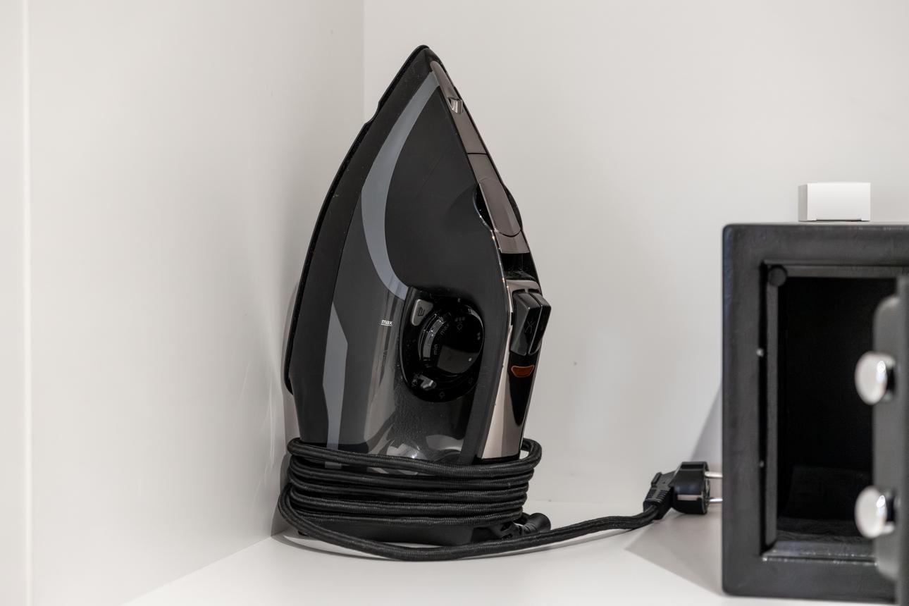 Modern black steam iron with wrapped cord displayed on a white shelf, providing essential garment care for travelers in hotel accommodation rooms